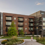Serene apartment courtyard at sunset with red and gray brick façades, balconies, trees, and landscaped walkways in front of The Hamilton apartments.