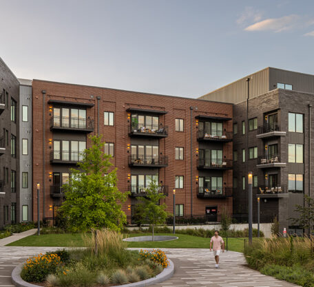 Serene apartment courtyard at sunset with red and gray brick façades, balconies, trees, and landscaped walkways in front of The Hamilton apartments.