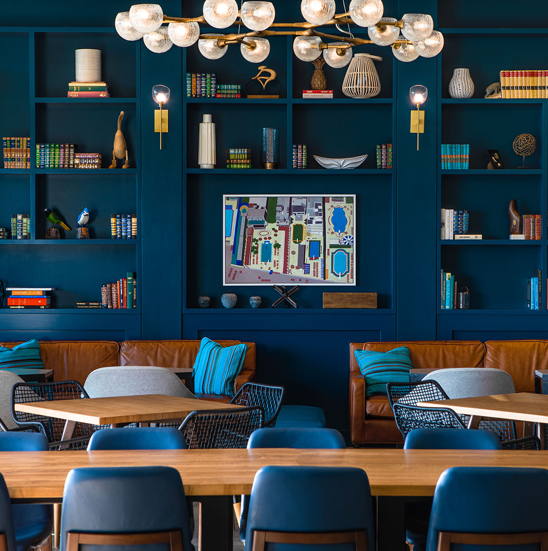 Close-up of a blue built-in bookshelf filled with books, art pieces, and decorative objects, positioned above a brown leather sofa with blue accent pillows.