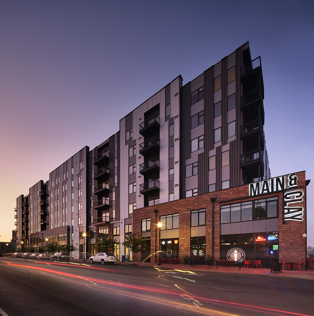 Vertical exterior shot of the Main & Clay building during twilight, emphasizing the dramatic height, clean architectural lines, and illuminated street activity.