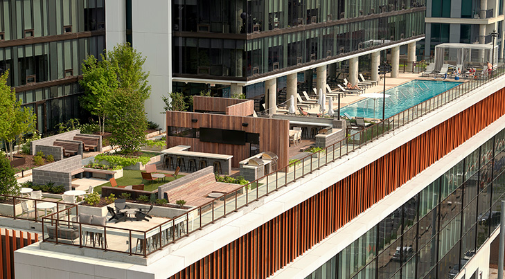 Expansive rooftop terrace with garden areas, lounge seating, grilling stations, and a long swimming pool, located atop a contemporary high-rise building.