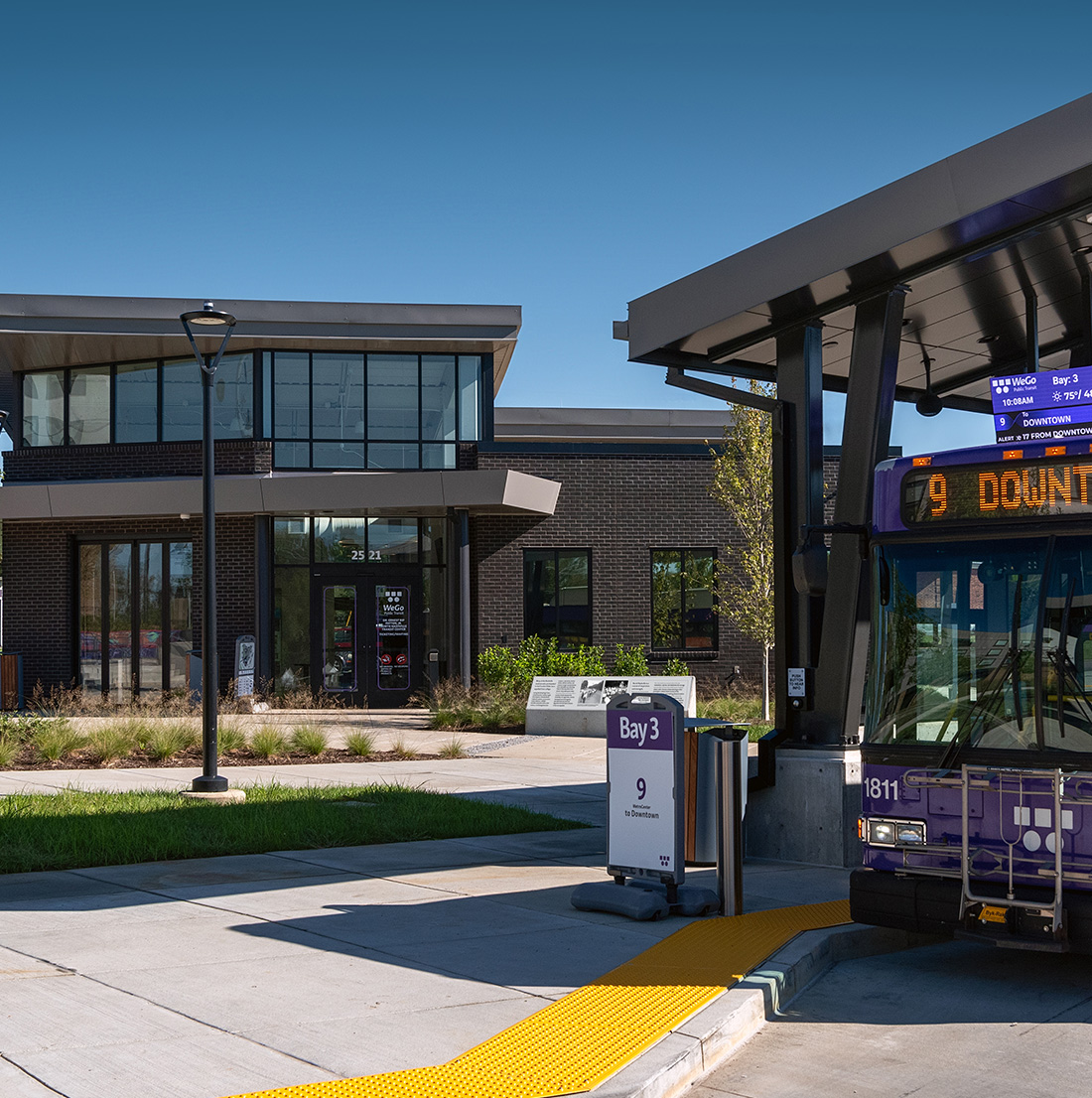 View of the transit center’s main entrance with a WeGo bus at Bay 3, digital signage above, and a landscaped pedestrian area in front.