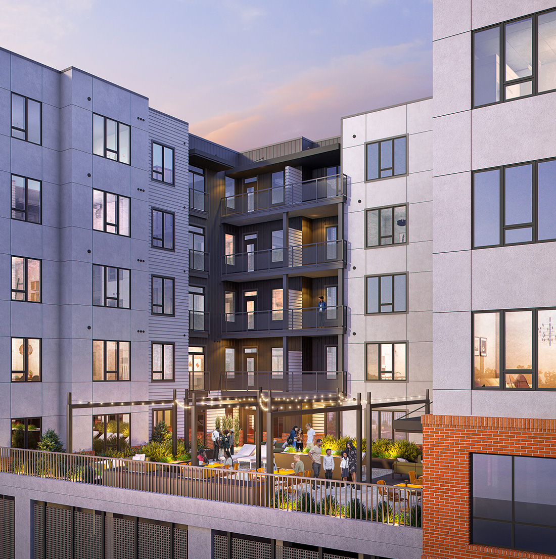 Dusk view of an elevated courtyard located between apartment buildings. Residents are gathered on a furnished patio beneath string lights, surrounded by landscaping, modern balconies, and large windows. The space creates a relaxed and inviting outdoor lounge atmosphere.